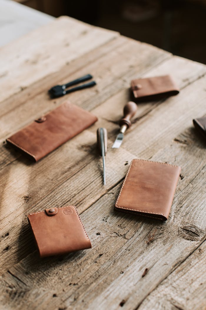 Close-up of handmade leather wallets with tools on wooden table.